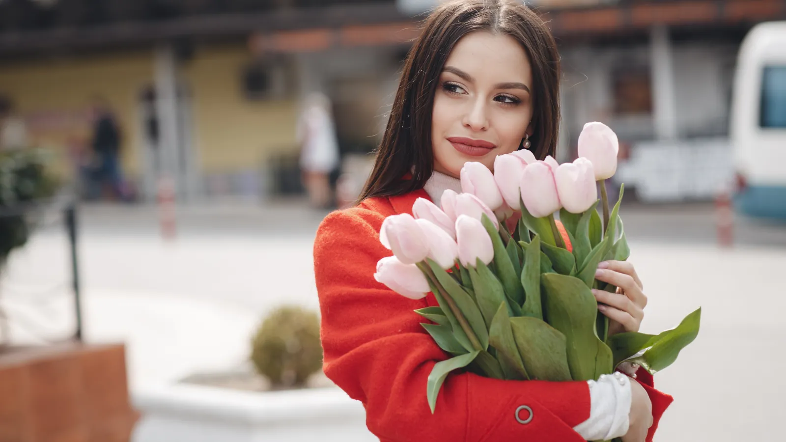 Uśmiechnięta kobieta z naręczem różowych tulipanów na wiosennej ulicy