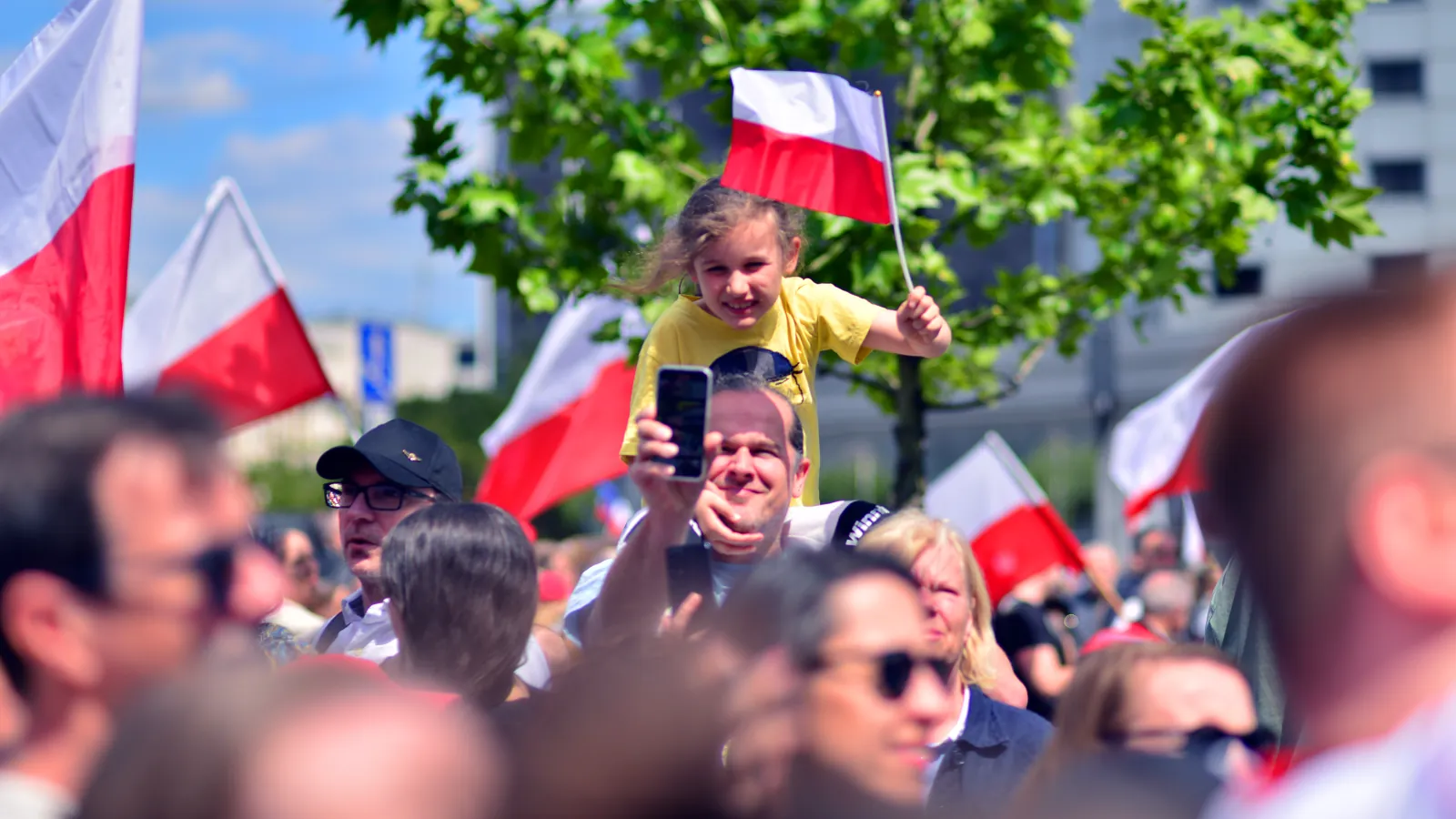 Dziewczynka machająca biało-czerwoną flagą w świątecznym tłumie